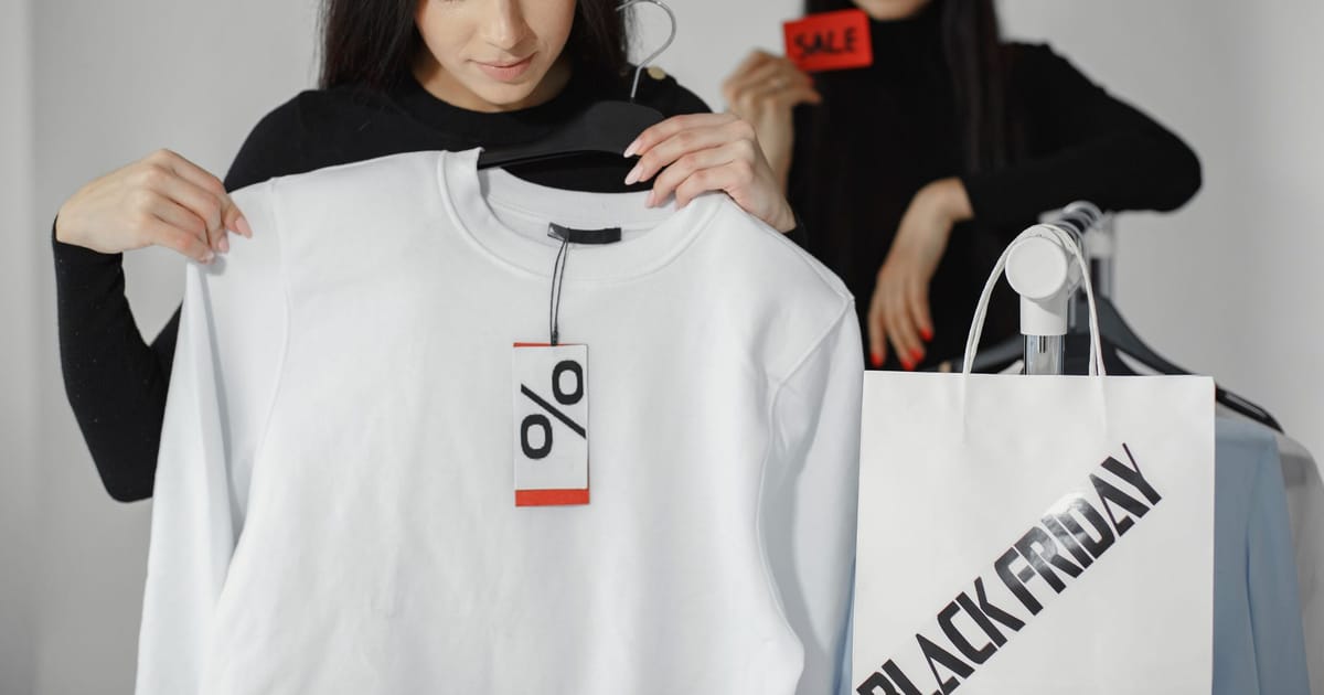 Mulher segurando uma blusa com etiqueta de porcentagem de desconto ao lado de uma sacola escrita Black Friday