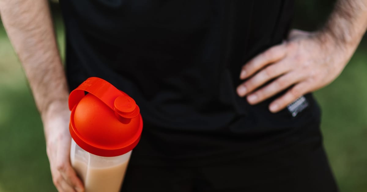 Pessoa de camiseta preta segurando uma coqueteleira com shake cremoso