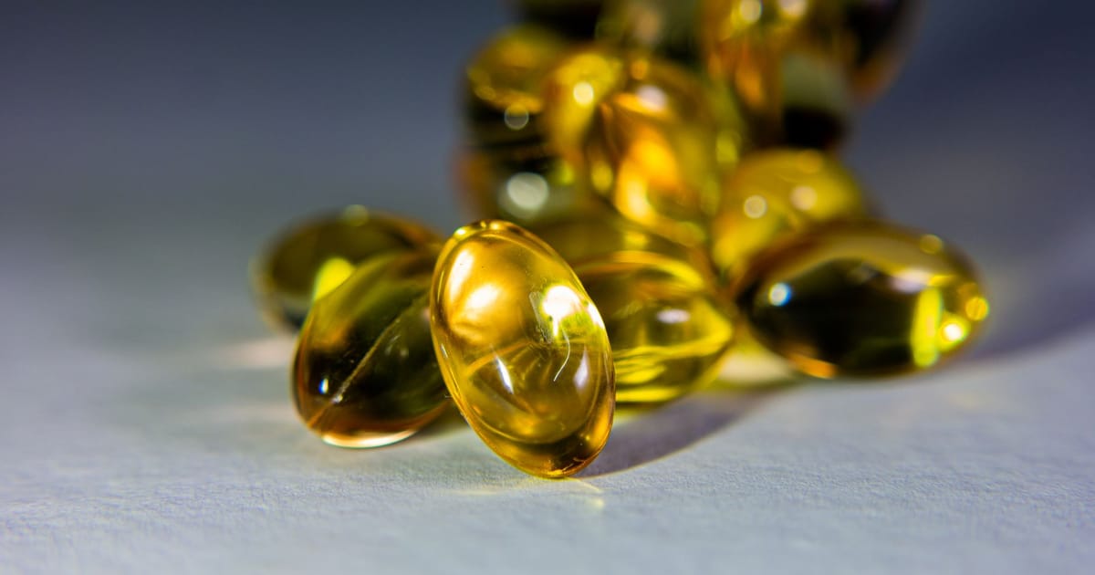 Cápsulas gel douradas de óleo de peixe em close sobre superfície acinzentada