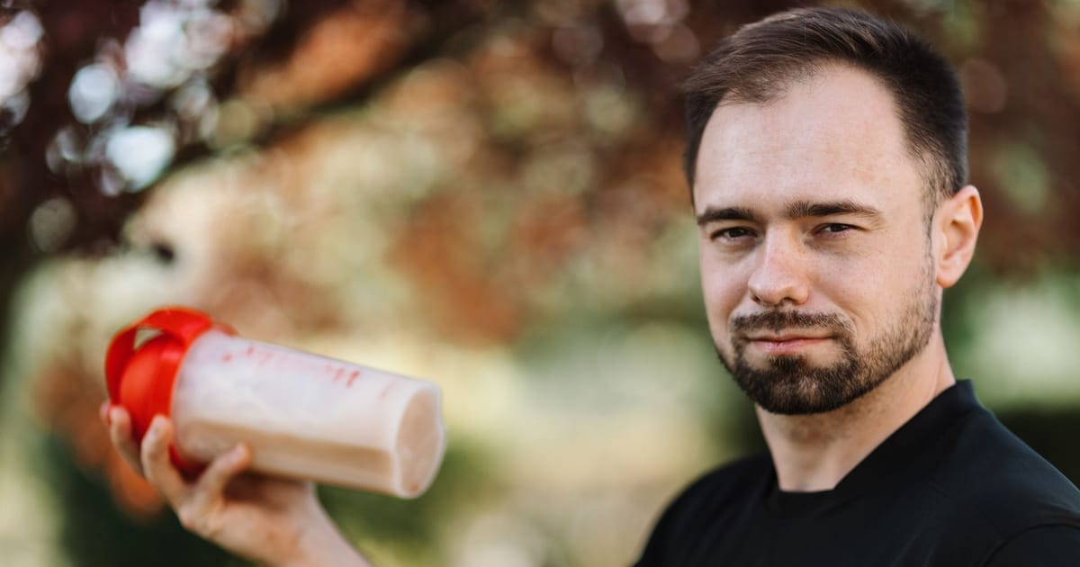 Homem de camiseta preta segurando uma coqueteleira com tampa vermelha cheia de shake